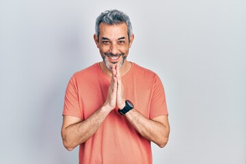 Handsome middle age man with grey hair wearing casual t shirt praying with hands together asking for forgiveness smiling confident.