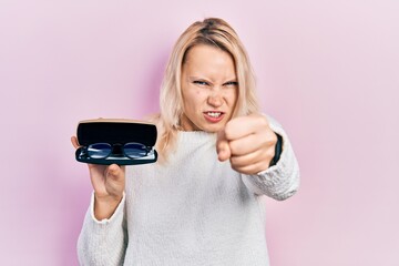 Fototapeta premium Beautiful caucasian blonde woman holding glasses in eyewear case annoyed and frustrated shouting with anger, yelling crazy with anger and hand raised