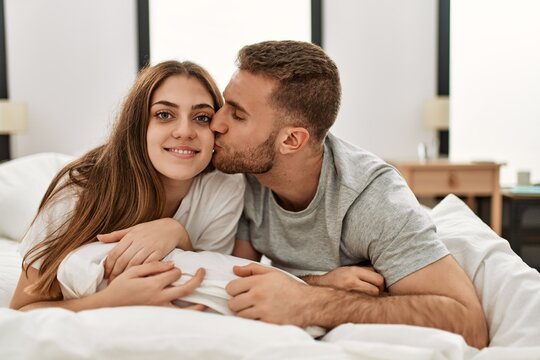Young caucasian couple smiling happy and kissing on the bed at home.