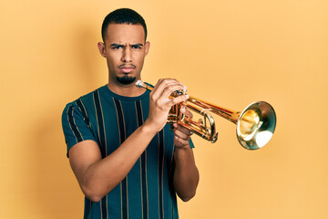Young african american man playing trumpet skeptic and nervous, frowning upset because of problem....