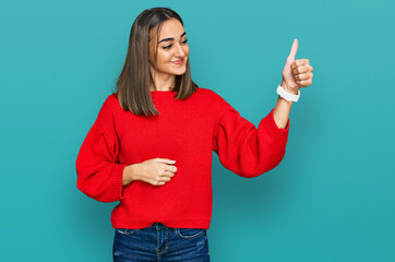 Beautiful brunette woman wearing casual winter sweater looking proud, smiling doing thumbs up gesture to the side