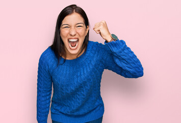 Young hispanic woman wearing casual clothes angry and mad raising fist frustrated and furious while...