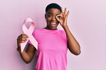 Young african american woman holding pink cancer ribbon smiling happy doing ok sign with hand on...