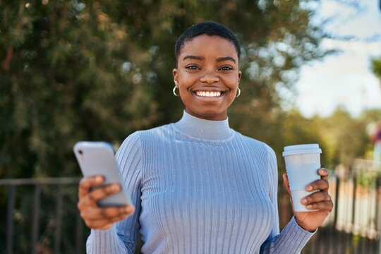Young african american woman using smartphone and drinking coffee at the city