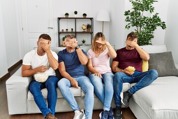 Group of middle age people sitting on the sofa at home covering eyes with hand, looking serious and...