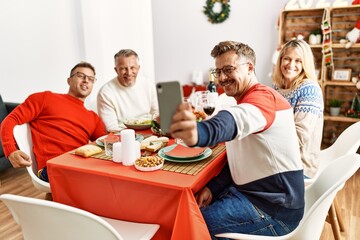Group of middle age friends smiling happy having christmas dinner and making selfie by the smartphone at home.
