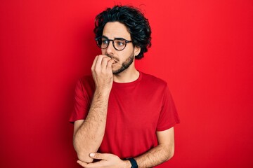 Fototapeta premium Handsome hispanic man wearing casual t shirt and glasses looking stressed and nervous with hands on mouth biting nails. anxiety problem.