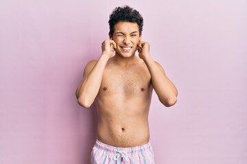 Fototapeta premium Young handsome man wearing swimwear shirtless covering ears with fingers with annoyed expression for the noise of loud music. deaf concept.