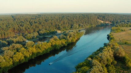 Aerial view above a beautiful landscape with a  river while sunset. Aerial view from drone flies over a beautiful summer landscape. Jet ski is floating on the river.