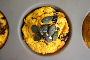 A gluten-free pumpkin cupcake sprinkled with pumpkin seeds lies with a gray silicone mold. top view. vegan sweets