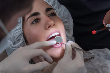 Mujer joven abre su boca y es revisada por el odontólogo con un espejo