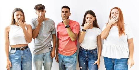 Fototapeta premium Group of young friends standing together over isolated background bored yawning tired covering mouth with hand. restless and sleepiness.