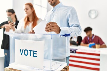 Young american voter man smiling happy putting ballot in voting box at vote center.
