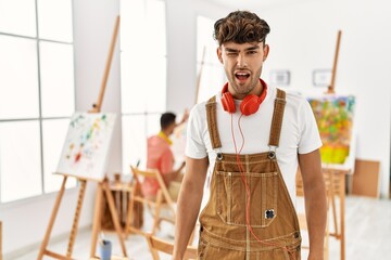 Young hispanic man at art studio winking looking at the camera with sexy expression, cheerful and happy face.
