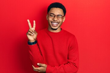 Young african american man wearing casual clothes and glasses smiling with happy face winking at the camera doing victory sign. number two.