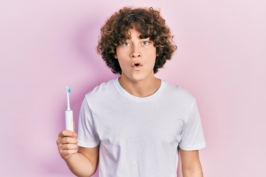 Handsome young man holding electric toothbrush scared and amazed with open mouth for surprise, disbelief face