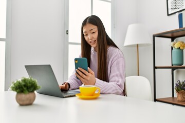 Young chinese girl using laptop and smartphone sitting on the table at home.