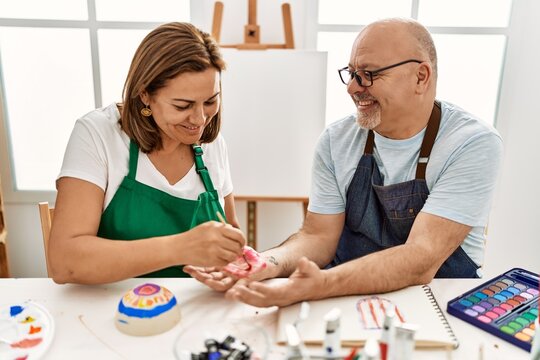 Middle age hispanic painter couple smiling happy painting palm hands at art studio.