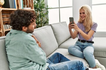 Fototapeta premium Young woman making picture of her boyfriend using smartphone at home