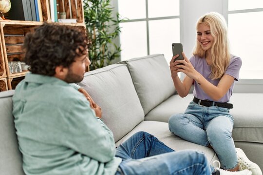 Young woman making picture of her boyfriend using smartphone at home