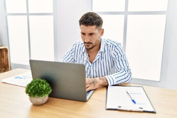 Young handsome man with beard working at the office using computer laptop skeptic and nervous, frowning upset because of problem. negative person.