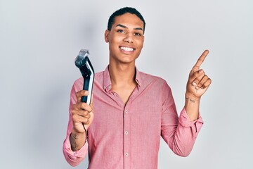 Young african american guy holding electric razor machine smiling happy pointing with hand and...