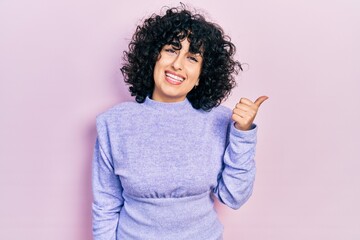 Young middle east woman wearing casual clothes smiling with happy face looking and pointing to the side with thumb up.
