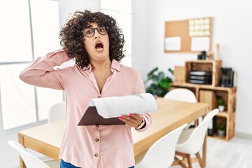 Young middle eastern woman wearing business style at office crazy and scared with hands on head, afraid and surprised of shock with open mouth