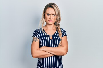 Beautiful young blonde woman wearing casual striped dress skeptic and nervous, disapproving expression on face with crossed arms. negative person.