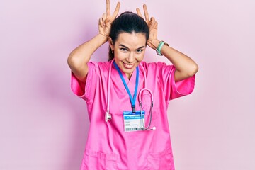Young brunette woman wearing doctor uniform and stethoscope posing funny and crazy with fingers on...