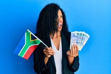 Middle age african american woman holding south african flag and rands angry and mad screaming...