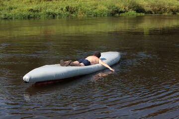 Happy person young curly brunette man on the lake rowing lying in an inverted tourist kayak having fun and sunbathing on a sunny summer day