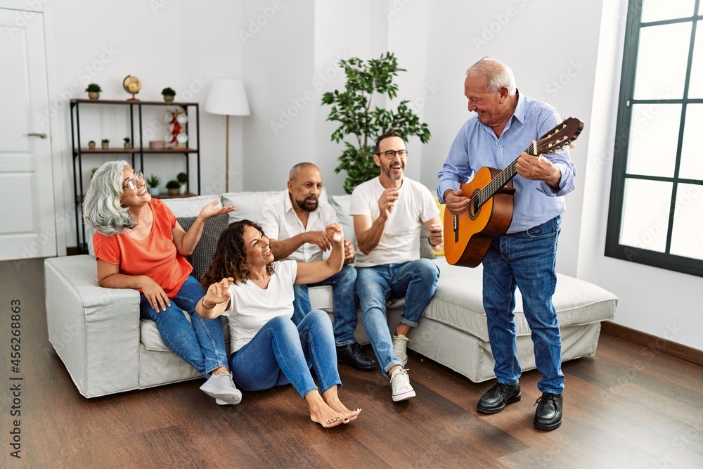 Poster Group of middle age friends having party playing classical guitar sitting on the sofa at home.