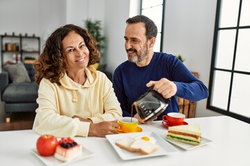 Middle age hispanic couple smiling happy sitting on the table having breakfast at home.