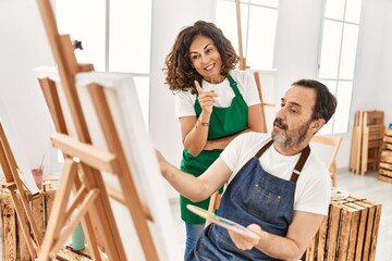 Middle age student and teacher smiling happy painting at art school.