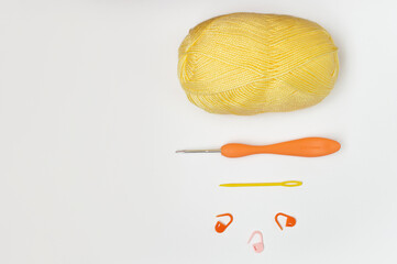 Top view of a skein of yellow yarn, crochet hook, needle and row counters. Colorful accessories for knitting on a gray background. Eco concept handmade. Flat lay.