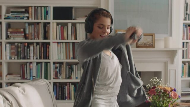 happy young woman dancing at home having fun enjoying funky hip hop dance moves practicing in living room using smartphone