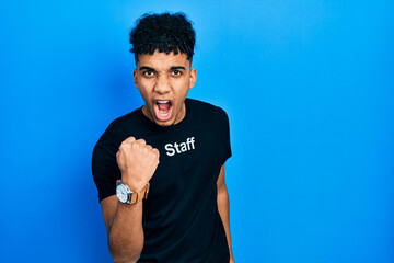 Young african american man wearing staff t shirt angry and mad raising fist frustrated and furious while shouting with anger. rage and aggressive concept.