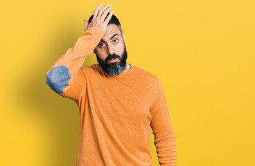 Hispanic man with beard wearing casual winter sweater surprised with hand on head for mistake,...