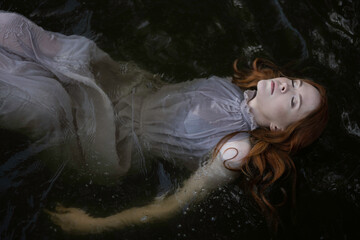 A red-haired girl in a gray dress lies on the black water