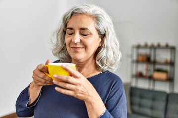 Middle age grey-haired woman drinking coffee standing at home.