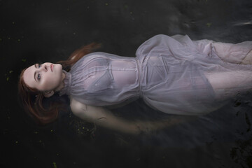 A red-haired girl in a gray dress floats on a black river