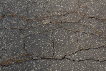 The texture of an asphalt road passing through the village. The road to the village. Dark-grey background texture of asphalt. Cracks in the asphalt. Destruction of the road