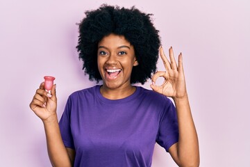 Young african american woman holding menstrual cup doing ok sign with fingers, smiling friendly gesturing excellent symbol