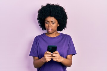 Young african american woman using smartphone typing message in shock face, looking skeptical and sarcastic, surprised with open mouth