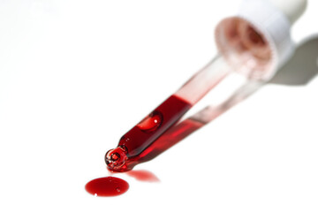 Liquid red oil serum drop in pipette isolated on white background. Retinol, aha acid, collagen...