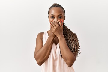 Black woman with braids standing over isolated background shocked covering mouth with hands for...