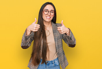 Young hispanic girl wearing business clothes and glasses success sign doing positive gesture with...