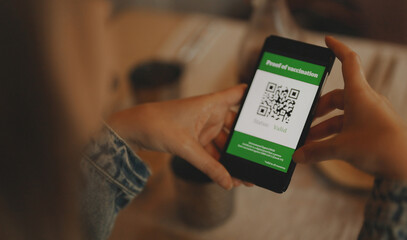 Woman in restaurant with certificate of immunization on smartphone. Status is valid.