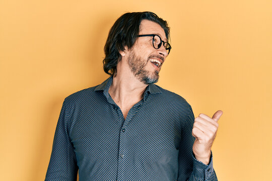 Middle age caucasian man wearing casual clothes and glasses pointing thumb up to the side smiling happy with open mouth